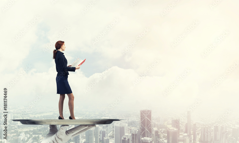 Obraz premium Attractive businesswoman on metal tray with red book in hands against cityscape background