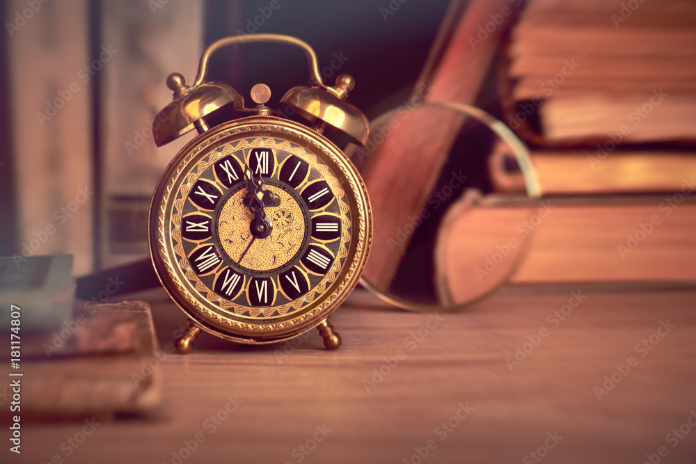Vintage alarm clock showing five to twelve among old books in study room