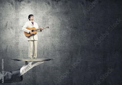 Businessman on metal tray playing acoustic guitar against concrete wall background