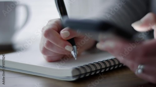 Closeup Of Woman Using Her Smartphone And Writing Notes In Her Notebook At Home 