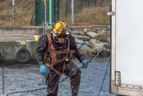 A diver with diving helmet searches for garbage on the harbor bottom in the harbor. He finds a bike thatis heavily covered with algae and shells and covered with seaweed. Keep our sea lake and river