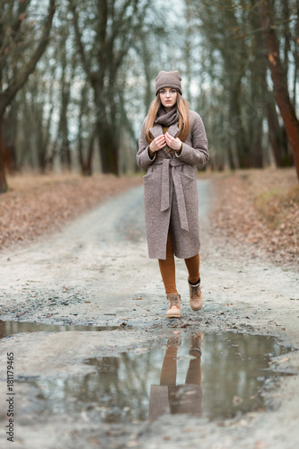 girl in a knitted hat and scarf at a puddle in the fall on nature. © makam1969