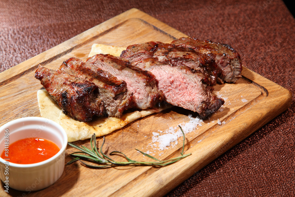 Medium-roasted steak cut into pieces on a wooden board with sauce and seasonings.
