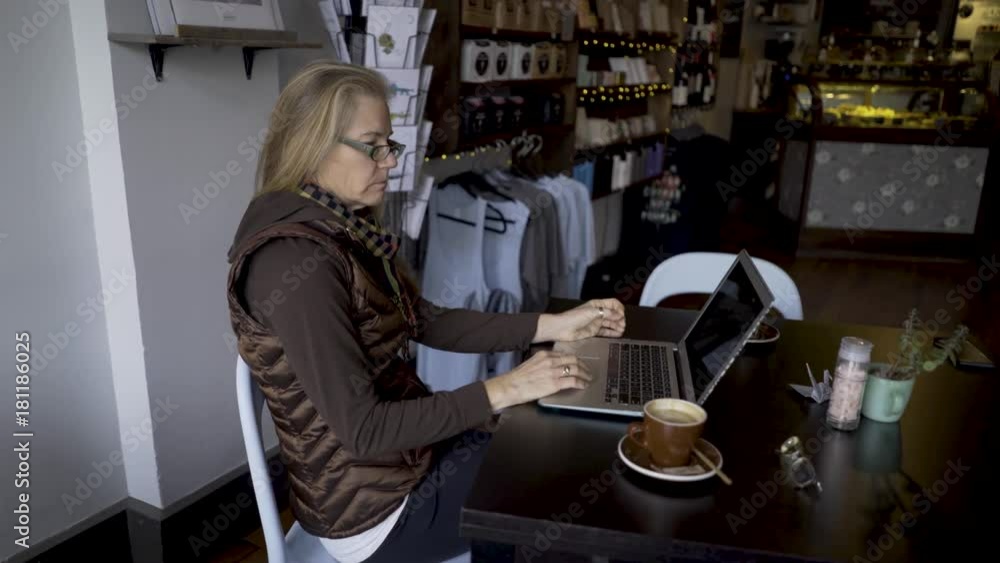 Static shot of a blonde caucasian woman on a laptop computer in a coffee bar cafe.