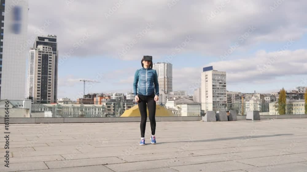 Excited young girl jumps winning VR video game with headset and hands up celebrate. mixed race model outdoors with cityscape background. Excited young girl jumps winning VR video game with headset and hands up celebrate. mixed race model outdoors with cityscape background.