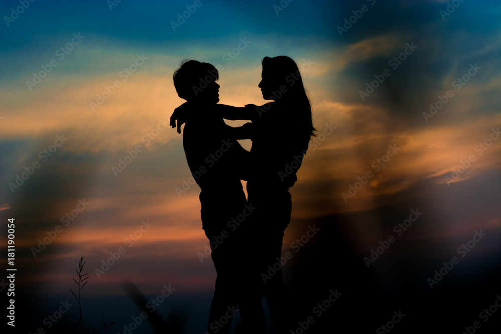 silhouette of romantic couple stand hugging and gaze into each other’s eyes on meadow at the sunset time . Have a beauty blue sky.