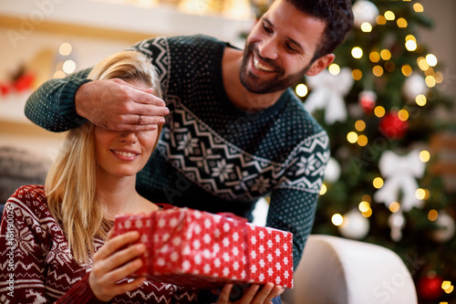 man covering woman's eyes with hands and giving gift box.