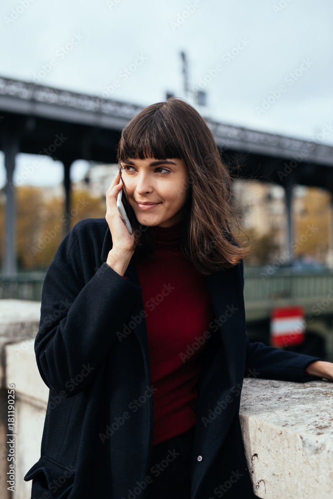 Girl walking and texting on the smart phone in the street wearing a black jacket in autumn