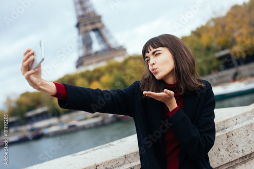 Tourist happy young woman taking selfie with smartphone and blowing air kiss near of Eiffel tower in Paris