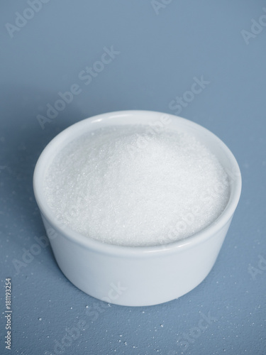 Schilderij op canvas Close up of portion of white sugar in small white bowl on blue background used a
