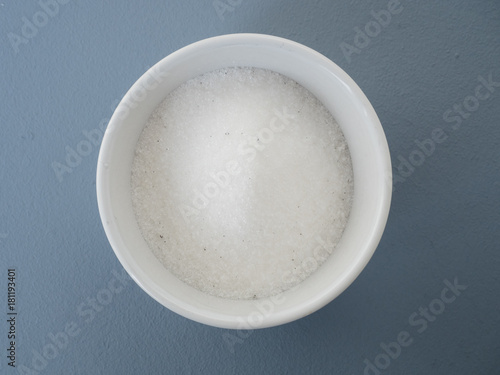 Close up of homemade vanilla sugar made from white caster sugar and a vanilla bean pod in small white bowl on blue background