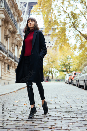 Beautiful amazing brunette woman in spring or fall stylish urban outfit walking on Paris street on with Eiffel background.