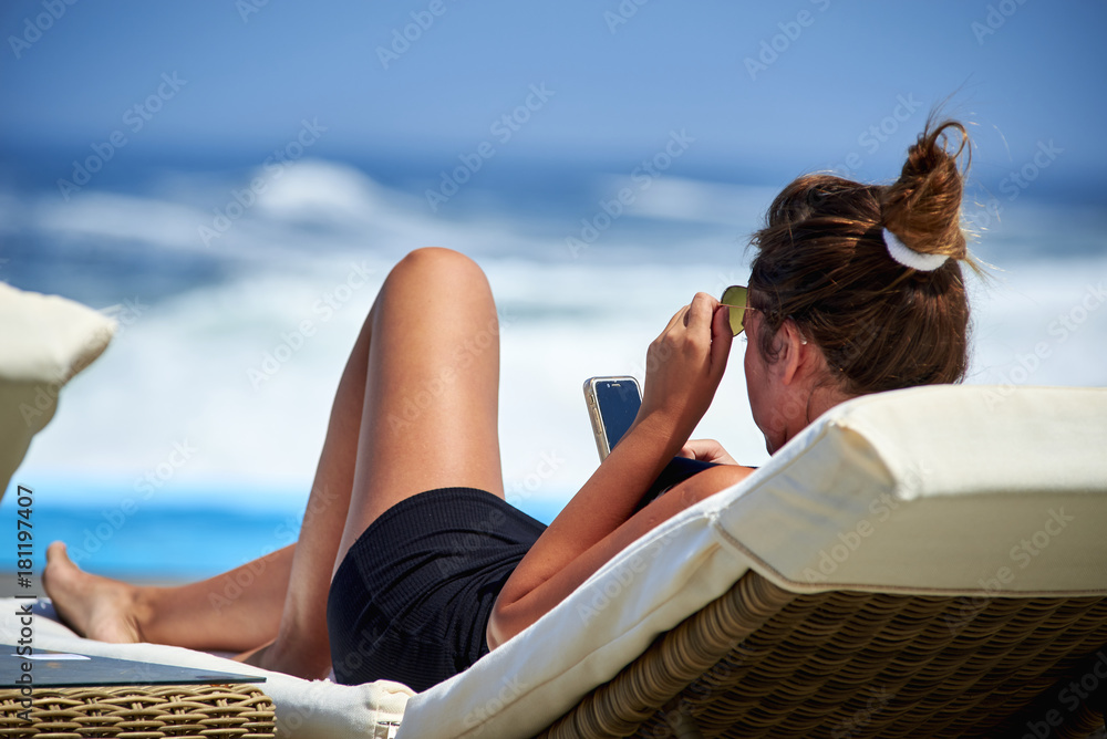atractiva y joven mujer tomando sol y viendo el celular - obrazy, fototapety, plakaty 