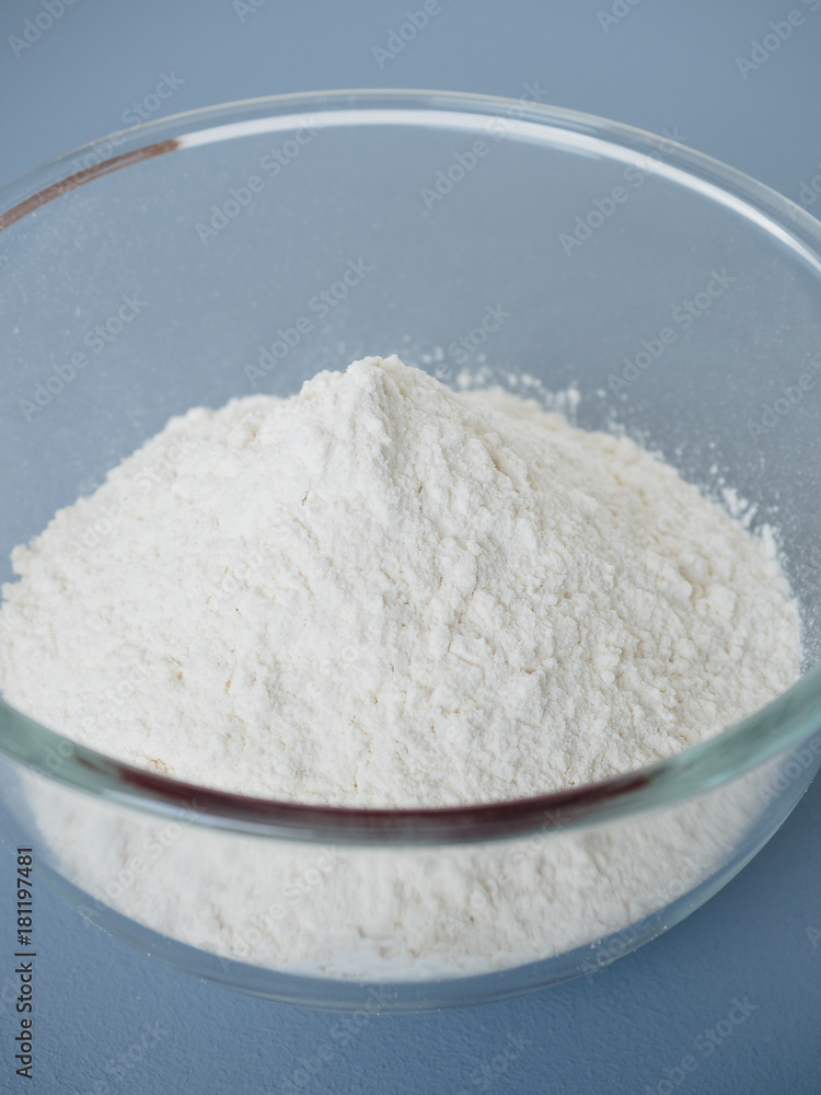 Close up shot of pile of plain white wheat flour in glass mixing bowl prepared for baking on blue background Close up shot of pile of plain white wheat flour in glass mixing bowl prepared for baking on blue background