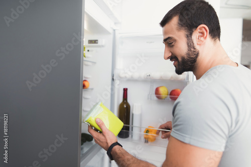 A sporty man stands in the kitchen and takes fresh vegetables from the refrigerator.