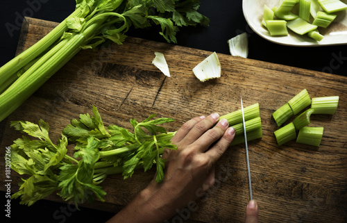 Aerial view of hands with knife cutting celery on wooden cut board photo