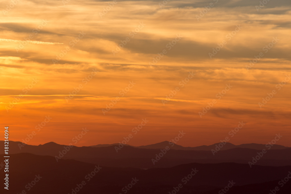 A silhouette of a mountain peak at sunset, under a big sky with beautiful red and yellow clouds