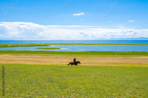 A horse rider on the shore of a large lake 