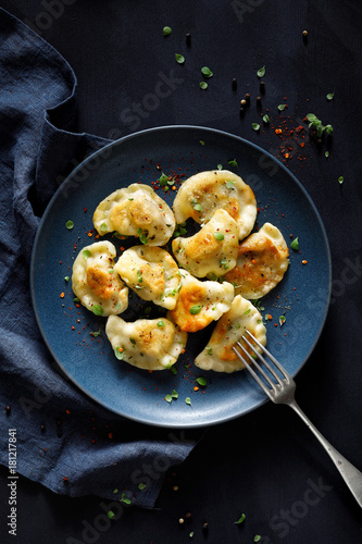 Dumplings, pierogi stuffed with meat sprinkled with fresh herbs on a blue plate, top view, black background. Traditional food in Poland