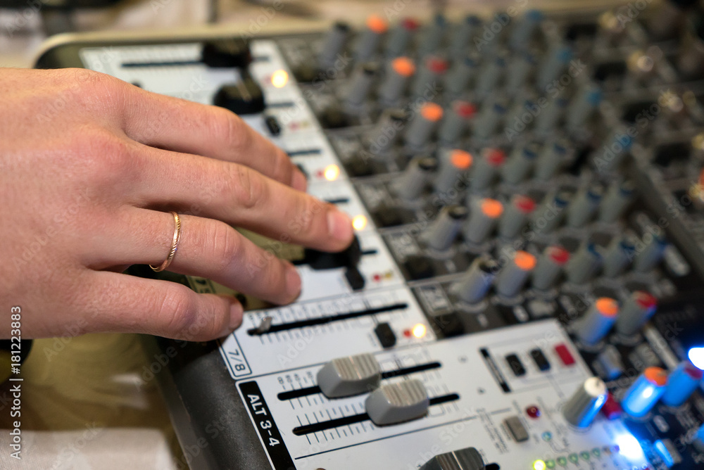 DJ working on a audiomixer at a nightclub. Close-up of hands adjusting quality of music using a knobs of the audio mixer
