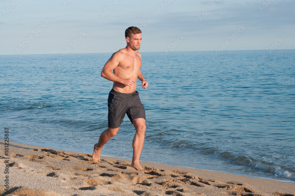 Muscular man barefoot running on beach