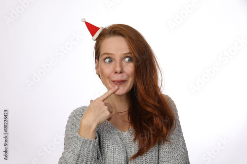 Hübsche rothaarige Frau mit kleiner Weihnachtsmütze überlegt