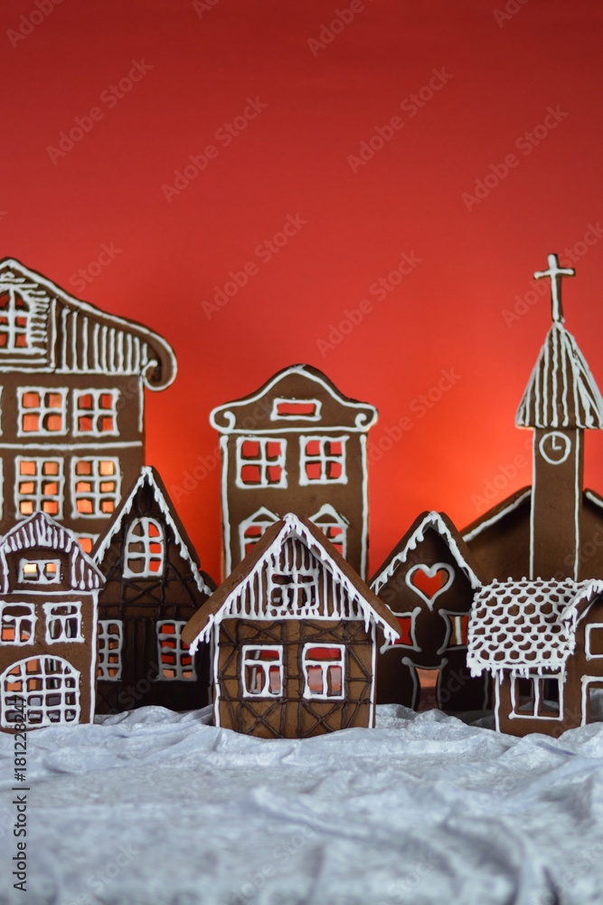 home made gingerbread village with church in front of red background on white snowlike velvet as christmas decoration