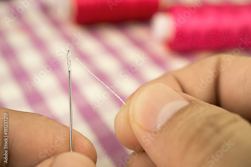 Finger holding sewing needle on the left and white thread on the right