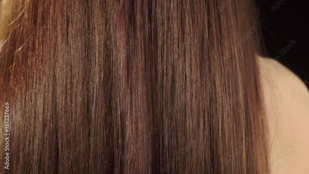 Beautiful woman with long brown straight hair rear view. Back view of a young brunette woman with bare shoulders wearing a black body hugging dress. Woman body part close-up. Beautiful woman with long brown straight hair rear view. Back view of a young brunette woman with bare shoulders wearing a black body hugging dress. Woman body part close-up.