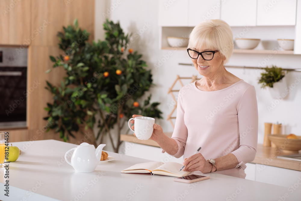 Cheerful aged woman making notes in the kitchen Cheerful aged woman making notes in the kitchen