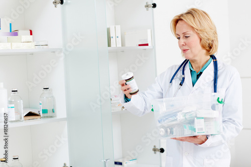 Female doctor looking through various pill-bottles and other medicine from plastic container