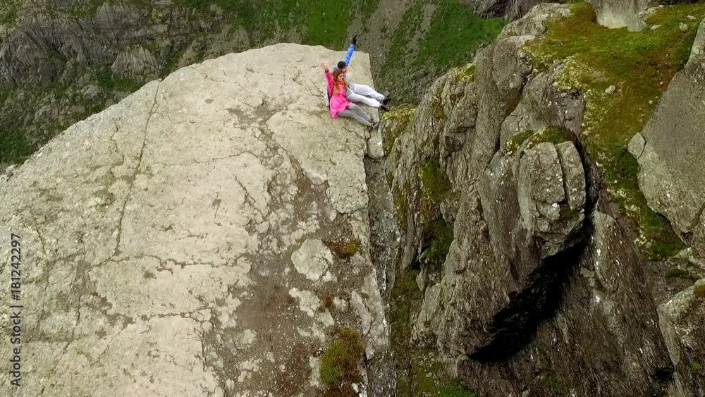 Trolltunga. Norway. The guy and the girl sitting on the edge of the Trolltunga. aerial vie. beautiful landscape of Norway Trolltunga. Norway. The guy and the girl sitting on the edge of the Trolltunga. aerial vie. beautiful landscape of Norway