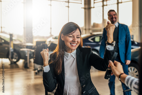 Cheerful young woman receiving the keys of her new car at car dealership.
