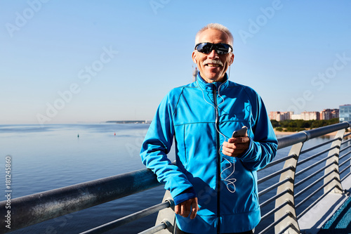 Contemporary sportsman with earphones and smartphone listening to music from playlist of favorites after training