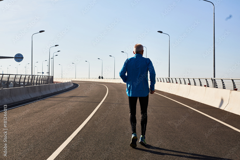 Rear view of man in leggins and sport jacket running along cycling roadway