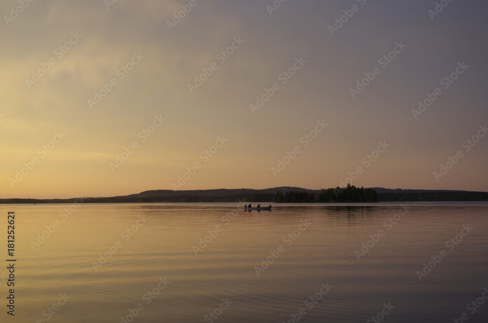 Fototapeta premium Peaceful evening landscape. Silhouette of people sailing in a boat over river after sunset. Gray misty background.
