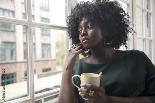 joven mujer negra toma café en la ventana photo