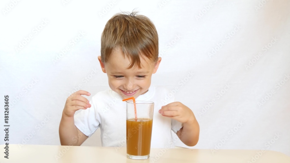 Little boy drinks juice through a straw while sitting at table - 2 Little boy drinks juice through a straw while sitting at table - 2