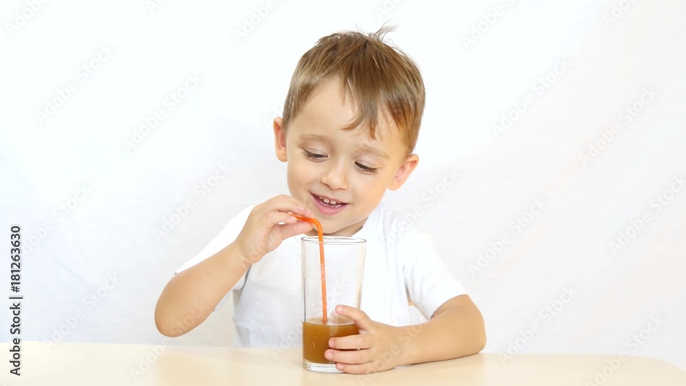 Happy child drinking juice through a straw for cocktails, sitting at a table and smiling on white background - 1 Happy child drinking juice through a straw for cocktails, sitting at a table and smiling on white background - 1