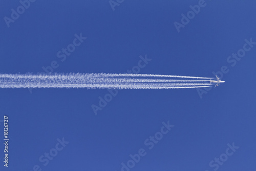 Airplane leaving condensation trails on a clear blue sky.