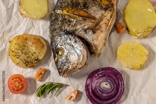 Tasty baked fish on baking paper. Baked sea bream with lemon, onion, herbs, cherry tomatoes, spices. Grilled delicious fish. Diet and healthy food. Top view