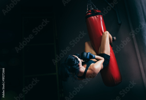Rear view of young beautiful sportswoman working at her abdominal muscules on a red punching bag on dark background. Sport, fitness, lifestyle, people and motivation concept. photo