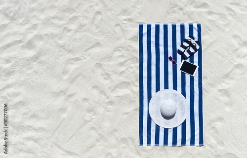 Top view of sandy beach with towel frame and summer accessories. Background with copy space and visible sand texture.