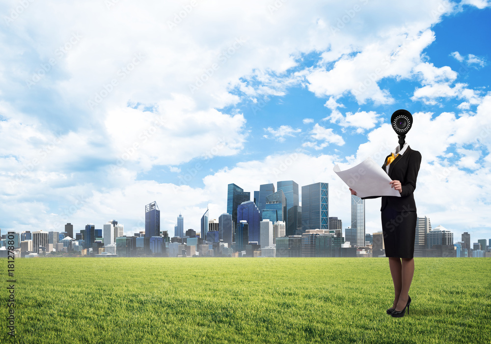 Camera headed woman standing on green grass against modern cityscape Camera headed woman standing on green grass against modern cityscape
