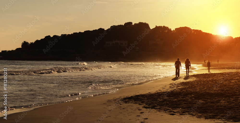 Silhouette of couple walking on the beach at sunset Silhouette of couple walking on the beach at sunset