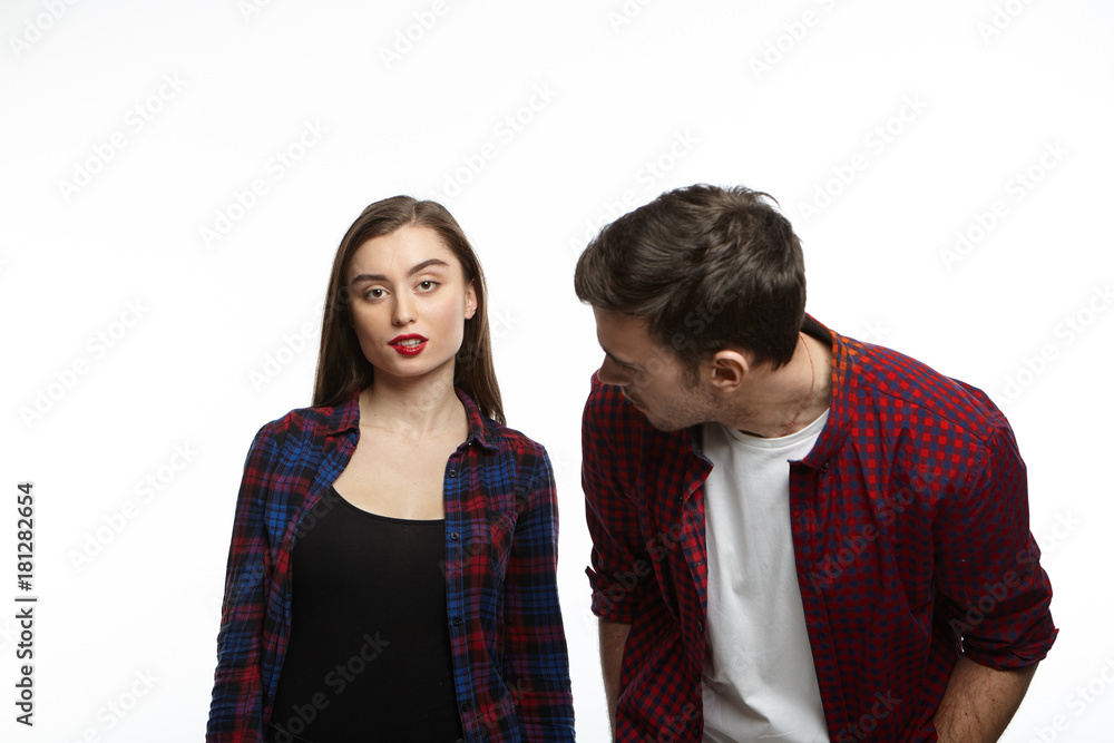 Horizontal shot of attractive young brunette female having confident facial expression, biting lips in playful flirtatious manner while her stylish boyfriend, bending and staring at her face Horizontal shot of attractive young brunette female having confident facial expression, biting lips in playful flirtatious manner while her stylish boyfriend, bending and staring at her face