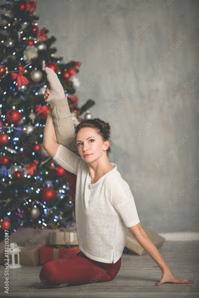 Beautiful flexible young woman is doing sports near christmas tree, sports and holiday concept Beautiful flexible young woman is doing sports near christmas tree, sports and holiday concept
