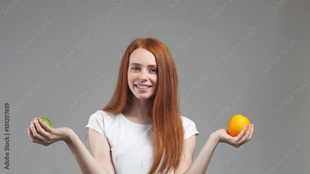 Beautiful redhead girl tries to choose orange or apple. Healthy food selection concept. Beautiful redhead girl tries to choose orange or apple. Healthy food selection concept.