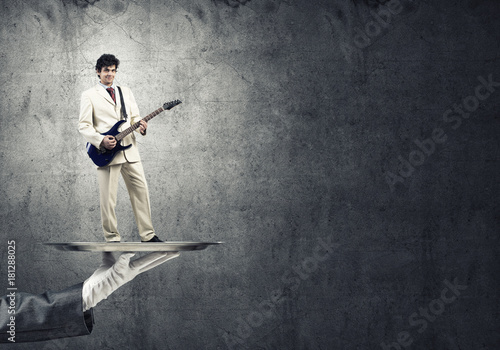 Businessman on metal tray playing electric guitar against concrete background