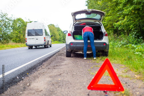 A girl is climbing in the trunk of a car. Emergency sign near the car © dima